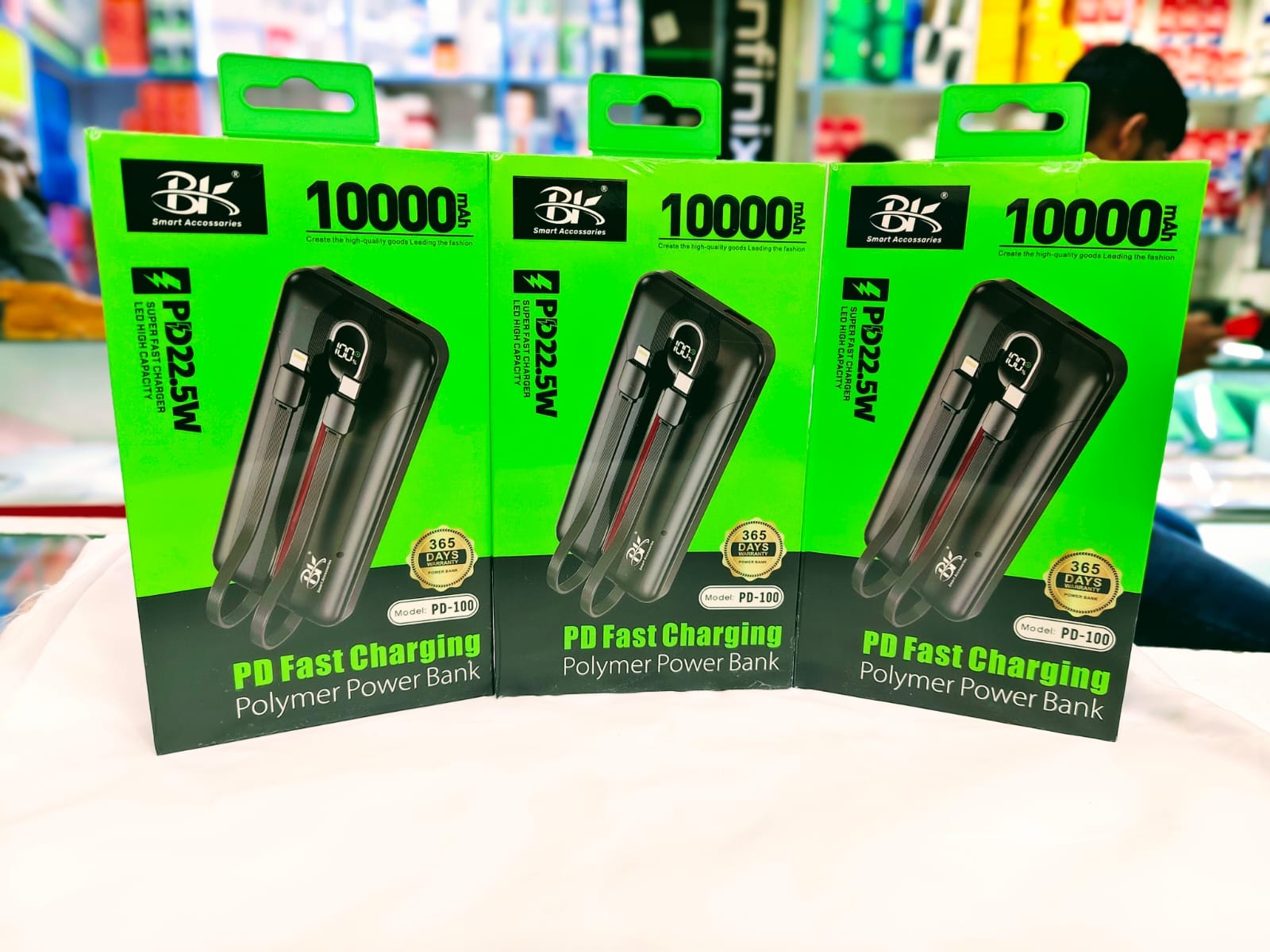 Three packages of BK 10000 PD Fast Charging Polymer Power Bank on a white surface with a blurred store background.
